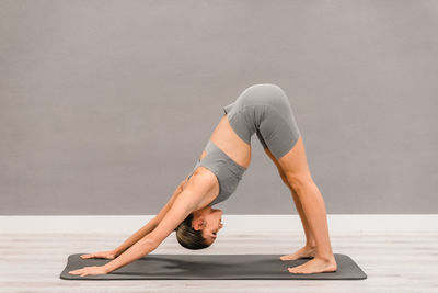 Side view of fit female in activewear standing barefoot on mat in adho mukha svanasana while practicing yoga and stretching body