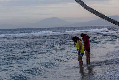 Side view of women standing at beach against sky during sunset