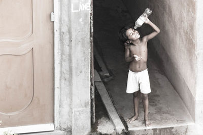 Full length of shirtless child holding water bottle by door