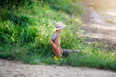 Cute european boy in hat plays hide and seek in park in grass, kid boy in summer forest