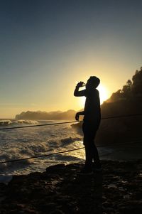 Silhouette man standing at beach against clear sky during sunset