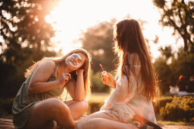 Happy girlfriends playing with bubbles in park during summer