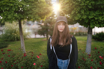 Portrait of beautiful young woman standing by flowering plants