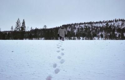 Rear view of man walking on snow covered landscape against sky