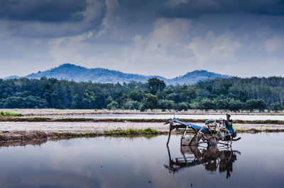 Abandoned tractor on wet agricultural field against cloudy sky