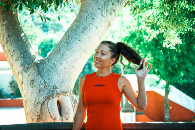 Happy woman standing by tree trunk