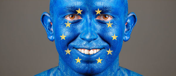 Close-up portrait of smiling man with european union flag body paint against gray background