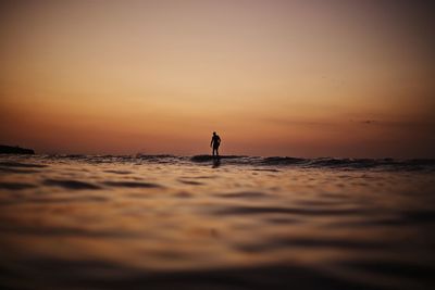 Silhouette man in sea against sky during sunset