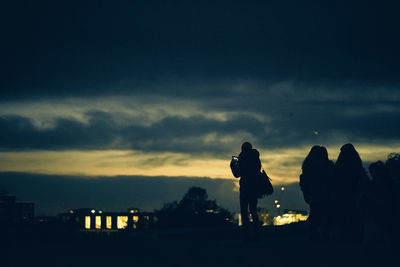 Silhouette people standing against cloudy sky during sunset