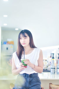 Portrait of young woman using mobile phone while standing against sky