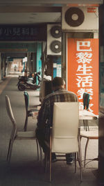 Rear view of people sitting on sidewalk cafe in city