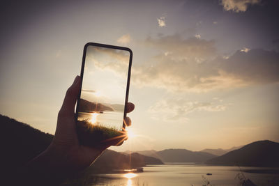 Person holding smart phone against sky during sunset