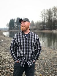 Smiling bearded man looking away while standing against lake