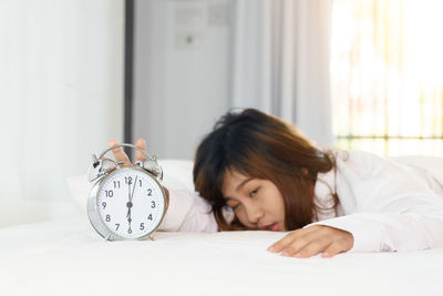 Tired woman reaching alarm clock while lying on bed at home