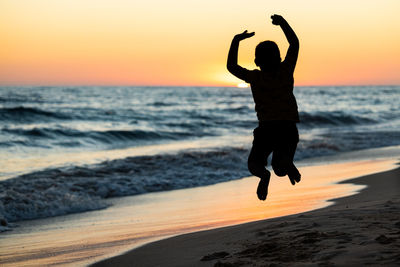 Little kid jumping on a beach at sunset