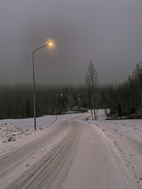 Snow covered road by trees against sky during winter