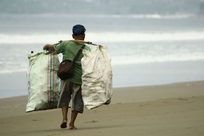 Rear view of man with carrying sacks on beach