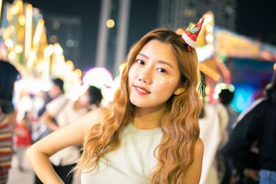 Portrait of smiling young woman wearing party hat standing in amusement park