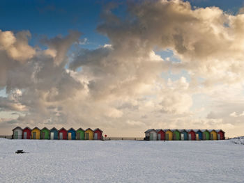 Huts at beach against cloudy sky