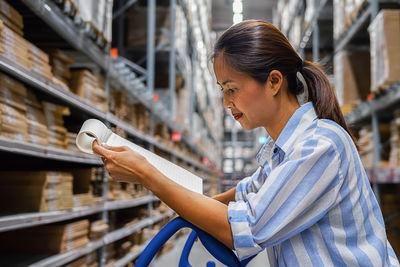 Woman checking list while standing in warehouse