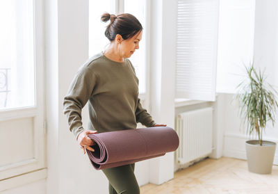 Attractive middle aged brunette woman in sportswear with yoga mat in the light studio