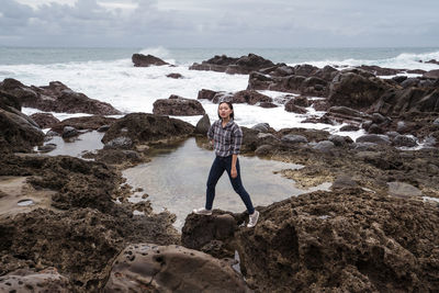 Full length of man standing on rock at beach against sky