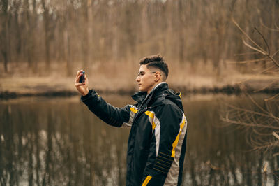 Side view of young man looking away while standing on lake