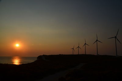 Silhouette wind turbines against sky during sunset