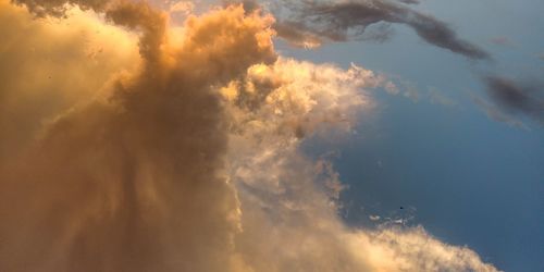 Low angle view of sunlight streaming through clouds during sunset