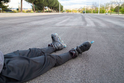 Low section of man wearing inline skates while sitting on road