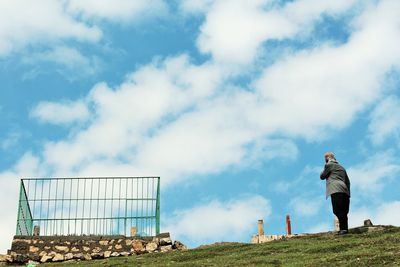 Low angle view of person standing on hill against cloudy sky during sunny day