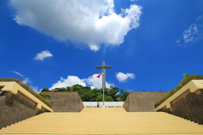 Low angle view of cross on steps against blue sky