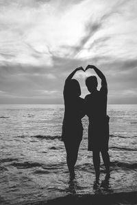 Silhouette couple making heart shape at beach against sky