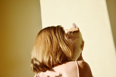 Rear view of woman with cat against wall