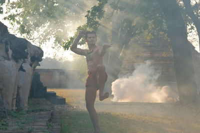 Side view of young man standing by trees