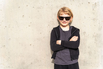 Portrait of young woman wearing sunglasses while standing against wall