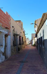 Footpath amidst buildings against blue sky