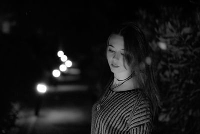 Young woman looking away while standing against black background