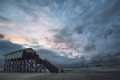 Lifeguard hut at beach against cloudy sky at dusk