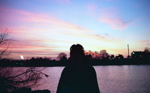 Silhouette woman standing by lake against sky during sunset