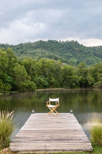 Folding chair on wooden plank footway at pond