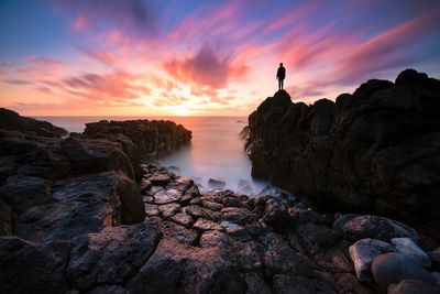 Rock formation at beach against sky during sunset