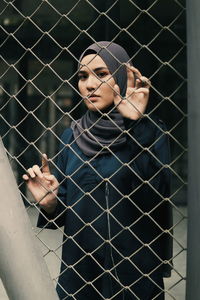 Portrait of young woman seen through metal fence