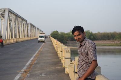 Side view portrait of mid adult man standing on bridge against clear sky