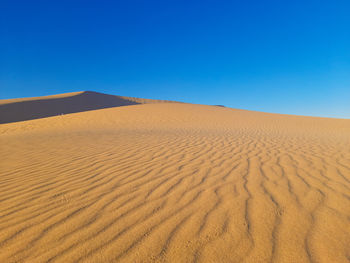 Sand dunes in desert against clear blue sky