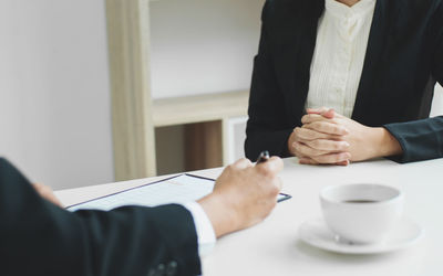 Midsection of colleagues by coffee cup on table