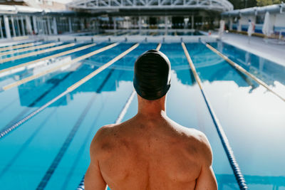 Shirtless male swimmer preparing to jump in swimming pool on sunny day