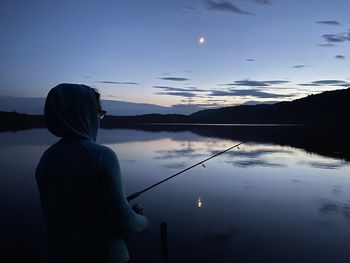 Rear view of silhouette man standing by lake against sky during sunset