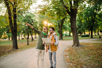 Young man gesturing while standing with friend holding map on road in park