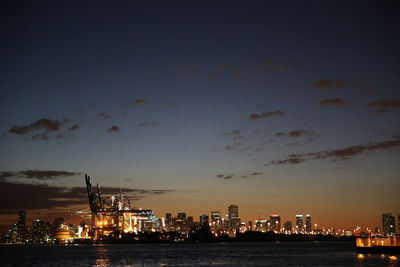 Illuminated miami cityscape by sea against sky at night